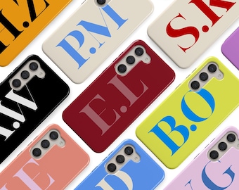 May include: A collection of colorful phone cases, each featuring a unique combination of initials in bold, contrasting colors. The cases are in various shades, including yellow, black, red, and pink, with the initials in blue, white, and red.