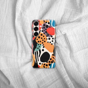 May include: A rectangular smartphone case featuring a vibrant abstract pattern of black, orange, red, and teal shapes, including solid circles, organic blobs, and small black dots, with a triple-lens camera cutout positioned on the upper left side.