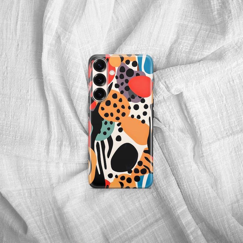 May include: A rectangular smartphone case featuring a vibrant abstract pattern of black, orange, red, and teal shapes, including solid circles, organic blobs, and small black dots, with a triple-lens camera cutout positioned on the upper left side.