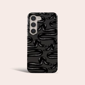 Peut inclure: Coque de téléphone noire avec un motif répété de serpents noirs sur un fond gris foncé. La coque a une découpe pour l'appareil photo avec trois objectifs.