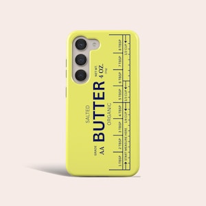 May include: A yellow phone case with a butter-themed design. The case features the words "SALTED AA BUTTER ORGANIC" and a measurement guide in tablespoons and cups. The net weight is listed as 4 oz.