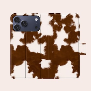 Peut inclure: Un étui de téléphone à motif de peau de vache marron et blanc. L'étui est conçu comme un folio, avec un rabat qui se replie sur l'écran du téléphone. L'étui a une bordure marron foncé et un aspect texturé, imitant l'apparence de la fourrure animale.