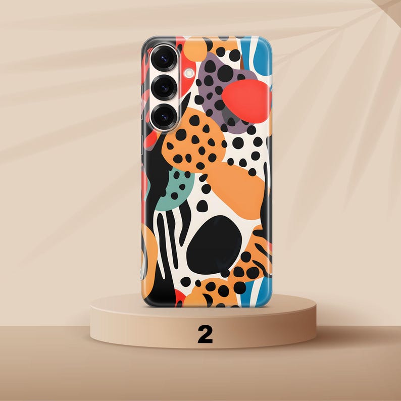 May include: A smartphone case featuring a vibrant abstract pattern of black, orange, red, and teal shapes on a cream background. The design includes various organic blobs and black polka dots, with a triple-lens camera cutout on the upper left side.