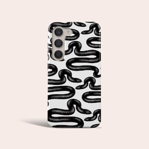 Puede incluir: Una funda de teléfono blanca con un patrón de serpiente negra. La funda tiene un recorte para la cámara en la parte posterior.