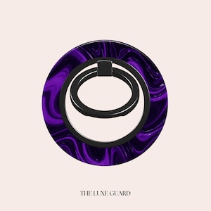 Könnte beinhalten: Ein Handy-Ringhalter mit einem wirbelnden lila und schwarzen Design. Der Ringhalter hat einen schwarzen Ring und eine kreisförmige Basis mit einem marmorierten lila Muster. Der Text "THE LUXE GUARD" befindet sich unten.