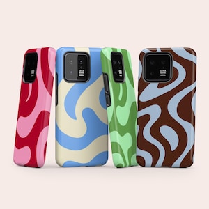 Op de afbeelding: Vier smartphonehoesjes met golvende, abstracte patronen. De eerste is rood en roze, de tweede crème en blauw, de derde lichtgroen en donkergroen, en de vierde bruin en lichtblauw. Elk hoesje heeft een zwarte camera-uitsparing met de tekst Leica.