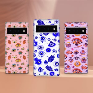 May include: Three phone cases with different designs featuring blue evil eyes and hamsa hands. The cases are white, pink, and purple.