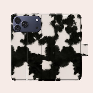 Peut inclure: Un étui de téléphone à motif de peau de vache noir et blanc. L'étui est de style folio, avec une fermeture magnétique. L'étui est conçu pour un smartphone avec plusieurs objectifs.