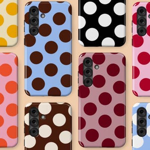 Puede incluir: Una colección de fundas para teléfonos inteligentes con varios diseños de lunares. Las fundas presentan una gama de colores, incluyendo azul, rosa, marrón, negro y amarillo, cada una adornada con lunares contrastantes. Las fundas tienen recortes para la cámara y ubicaciones de botones.