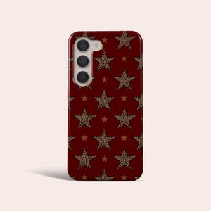 May include: A smartphone case with a burgundy background and a repeating pattern of leopard print stars and smaller brown stars. The case has a camera module with three lenses.