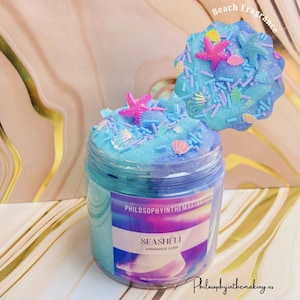 Peut inclure: Un pot de slime fait à la main en forme de coquillage avec un parfum de plage. Le slime bleu est décoré d'étoiles de mer roses, de paillettes en forme de coquillages et de petites coquilles. Le pot porte l'étiquette "Seashell Handmade Slime".