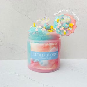 以下が含まれることがあります： ピンクとブルーの渦巻き状のスライムが入った透明なプラスチック容器。虹色のビーズと星や月の形をしたスプリンクルがトッピングされています。ラベルにはPHILOSOPHYINTHEMAKING、CLOUD STORM、HANDMADE SLIME、PHILOSOPHYINTHEMAKINGUSと記載されています。