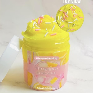 以下が含まれることがあります： 「Strawberry Lemonade」とラベルされた、白い蓋が付いた黄色のスライムの瓶。スライムは黄色のフロスティングとスプリンクルでトッピングされています。瓶には「Philosophyinthemaking」というテキストが入ったピンクと白のラベルが付いています。