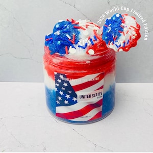 May include: A jar of United States slime, featuring red, white, and blue layers and toppings. The jar has a label with the American flag and the text "United States Slime". The image also includes the text "2026 World Cup Limited Edition".