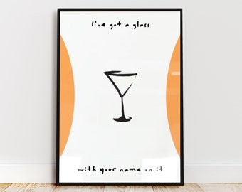 Pode incluir: Uma impressão de arte de parede emoldurada com fundo branco e dois painéis laterais verticais laranja. No centro, há uma ilustração desenhada à mão de uma taça de martini preta. O texto diz: I've got a glass with your name on it.