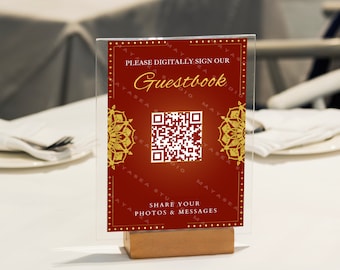 Pode incluir: Uma placa vermelha e dourada com o texto "Por favor, assine digitalmente nosso livro de visitas" e um código QR. A placa está em um suporte de madeira e está sobre uma mesa branca.