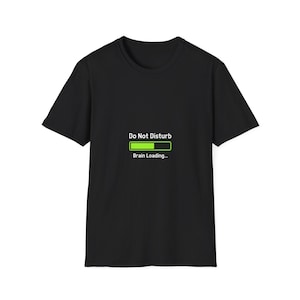 May include: Black t-shirt featuring the text "Do Not Disturb" above a green loading bar graphic that reads "Brain Loading...". The tee shirt has a crew neck and is likely made of cotton.