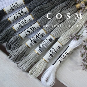 May include: A collection of gray and white embroidery floss spools with barcodes and numbers, including 155, 2154, 154, 153A, 152A, 2151, 151, and 2500. The spools are arranged in a row on a white wooden surface. The text "COSMO premium embroidery threads" is visible on the top of the image.