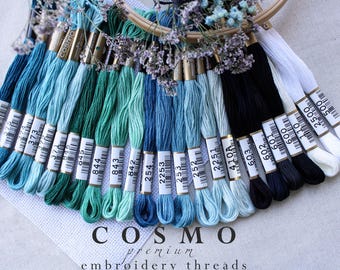May include: A collection of embroidery floss spools in shades of blue, green, and black. The spools are labeled with numbers, including 376, 373, 645, 844, 843, 842, 254, 2253, 253, 252, 2251, 603, 602, 601, 009, 110, 2500, and 500. The text "COSMO premium embroidery threads" is printed below the spools.