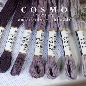 May include: Seven spools of Cosmo embroidery thread in shades of purple and gray. The spools are labeled with the numbers 766, 765, 764, 763, 2762, 762, and 761.