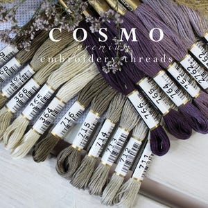May include: Assortment of embroidery floss spools in shades of brown, beige, gray, and purple. The spools are labeled with numbers, including 369, 368, 366, 365, 364, 716, 715, 714, 713, 712, 711, 766, 765, 764, 763, 2762, 762, 761. The brand name "COSMO premium embroidery threads" is visible on the label.