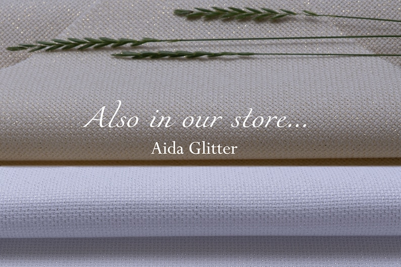 K&ouml;nnte beinhalten: Zwei St&uuml;cke Aida-Stoff, eines wei&szlig; und eines mit einem dezenten Glitzer-Finish. Der Text "Also in our store... Aida Glitter" ist auf den Stoff gedruckt.