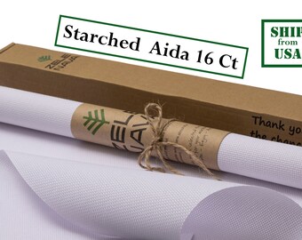 May include: A roll of white starched Aida fabric, 16 count, wrapped in brown paper with a green tree logo and tied with twine. The fabric is packaged in a brown cardboard box with the text "Starched Aida 16 Ct" and "Thank you for the chance to..." printed on it.