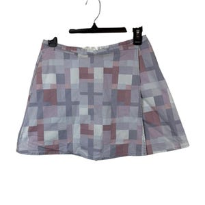 May include: A wrap-style skirt with a geometric pattern in shades of gray, lavender, and burgundy. The skirt is hanging on a black hanger against a white background. The fabric appears to be lightweight.