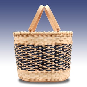May include: A woven basket with a black and natural woven pattern and wooden handles. The basket is oval shaped and has a natural wood finish.