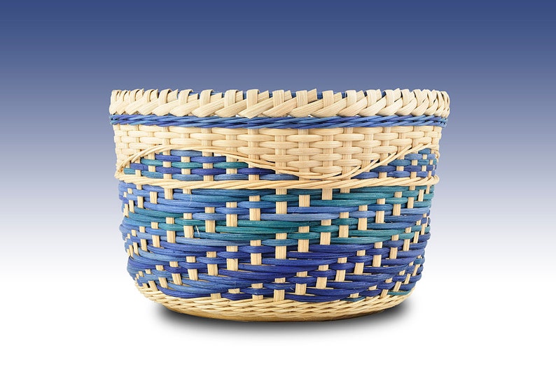 May include: A woven basket with a blue and green pattern. The basket is made of natural materials and has a round shape.