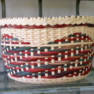 May include: A woven basket with a red, white, and brown pattern. The basket is made of natural materials and has a round shape.