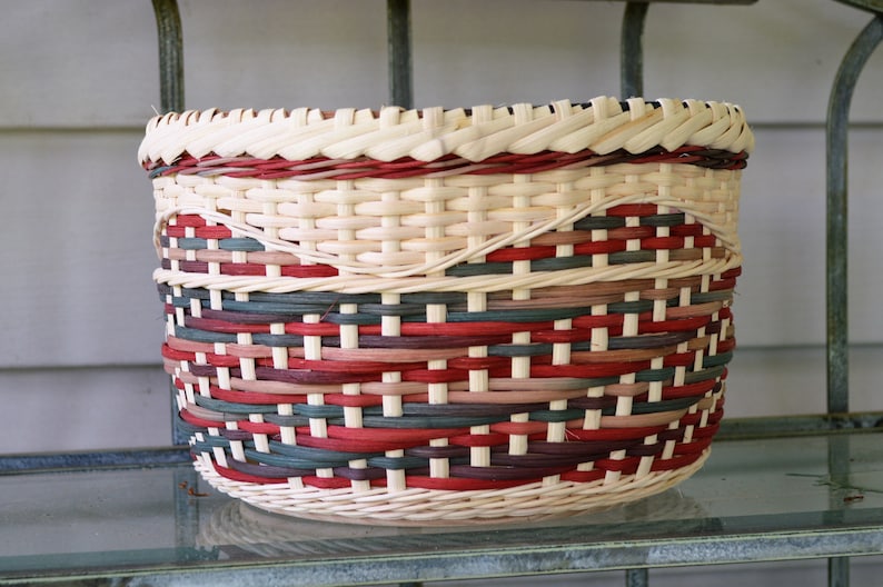 May include: A woven basket with a red, white, and brown pattern. The basket is made of natural materials and has a round shape.