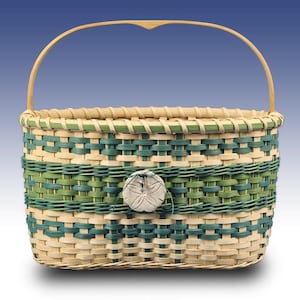 May include: Woven basket with a handle, featuring a rectangular shape and a decorative button. The basket is made of natural and green-colored woven materials. The handle is made of a light-colored wood.