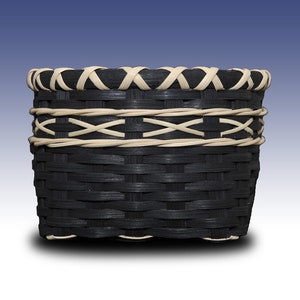 May include: A black woven basket with a white woven rim and accents. The basket is round and has a wide opening.