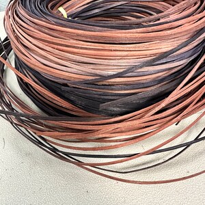 May include: A close-up of a coil of natural woven rattan, with a mix of brown and black colors. The rattan is used for crafting and weaving.