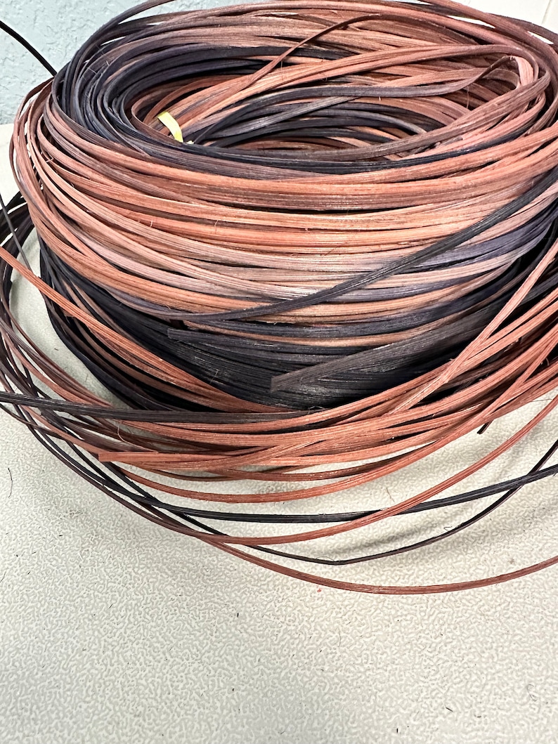 May include: A close-up of a coil of natural woven rattan, with a mix of brown and black colors. The rattan is used for crafting and weaving.