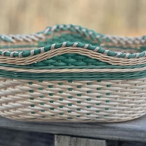 May include: A rectangular woven basket with a scalloped rim. The basket features a combination of cream, green, and tan woven materials. The basket is made of woven material and is suitable for storage or display.