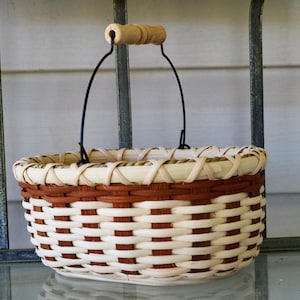May include: A woven basket with a brown and white pattern and a black metal handle with a wooden knob. The basket is sitting on a glass surface.