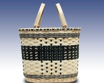 May include: Woven basket with a rectangular base and a pair of wooden handles. The basket features a natural, light-colored weave with a horizontal band of black weave. The rim is also trimmed with black and natural weave.