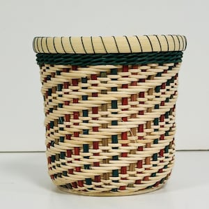 May include: A woven basket with a green, red, and brown pattern. The basket is made of natural materials and has a round shape.