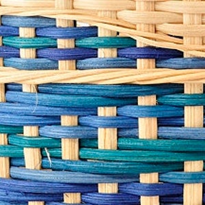 May include: Close-up of a woven basket with a pattern of blue and teal stripes. The basket is made of natural materials and has a light brown color.