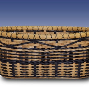 May include: An oval-shaped woven basket featuring a pattern of natural light tan and dark black reeds. The rim is reinforced with a thick, light-colored band secured by a crisscross stitch pattern, creating a structured and durable container.