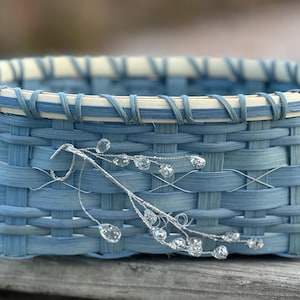 May include: A blue woven basket with a white rim and a silver twig with crystal-like beads.