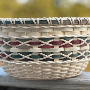 May include: A woven basket with a natural brown color and a decorative pattern of red, green, and brown woven strips. The basket is round and has a wide opening.