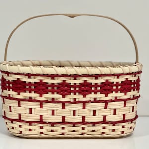 May include: A woven basket with a red and white pattern and a wooden handle.