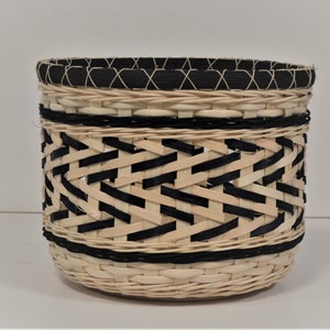 May include: A woven basket with a black and natural colored design. The basket is round and has a wide opening.