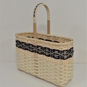 May include: A woven basket with a natural wood handle and a black and gray geometric pattern around the top.