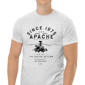 May include: Light grey t-shirt with a black graphic of an Apache helicopter. The text on the shirt reads "SINCE 1975 APACHE ARMY DEPT. UNITED STATES ARMY" and "THE DESIGN OUTLAW". The shirt is made of a soft, comfortable material.