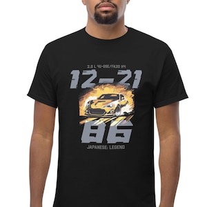 Peut inclure: T-shirt noir avec un motif de voiture de sport jaune avec des flammes et le texte "12-21 86 JAPANESE LEGEND 2.0 L 4U-GSE/FA20 HP"