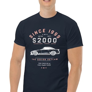 May include: A navy blue t-shirt with a white graphic design featuring a car and the text "SINCE 1999 MOTOR DEPT. S2000 TAKAREZAWA, TOERISI JAPAN THE DESIGN OUTLAW YOUR PURVEYOR OF FINELY CRAFTED GOODS"